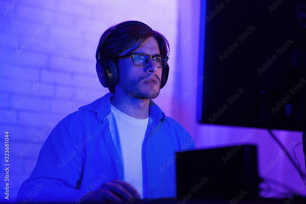 Poster concentrated hacker working on pc computer sitting indoor, low light