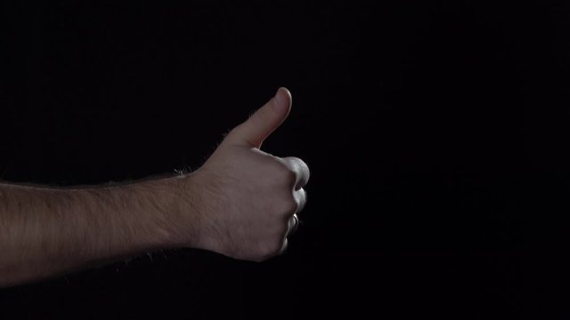 Man's hand shows humb up gesture on black background. Blackout, 4K