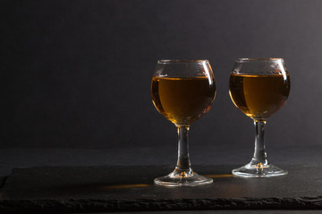 Glass of whiskey on a black stone slate board on black background. Side view, low key, copy space.