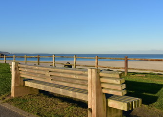 Fototapeta na wymiar Wooden bench on a beach promenade with morning light and blue sky. Arteixo, Coruña, Galicia, Spain.