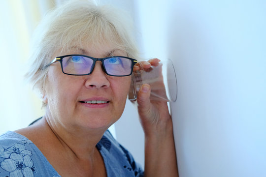 A Woman Uses A Glass Cup To Listen To Neighbors Through The Wall