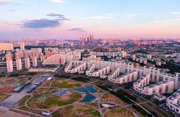 Top view of the city of Moscow and city leisure park, in the frame a green field and paths, a lake. In the background are beautiful houses and a large business center. Aerial photography