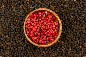 Spice background, Background made of many whole black peppercorns and a wooden bowls filled with red peppercorns , extreme close up, top view