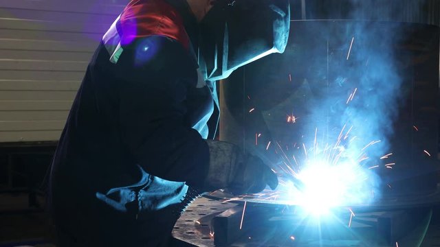 Man in the shop perform metal work with bright sparks from welding equipment