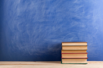 Education and reading concept - group of books on the wooden table, blue blackboard background. Teachers desk