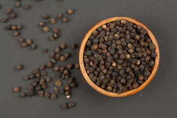 A small wooden bowl filled with black peppercorns on a black background