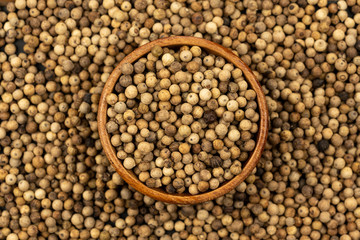 Spice background, Background made of many whole white peppercorns and a small wooden bowl, filled with white peppercorns, close up, top view