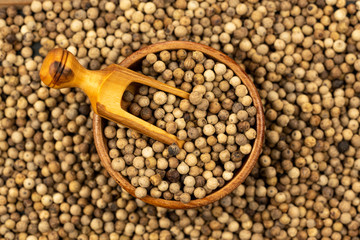 Spice background, Background made of many whole white peppercorns and a small wooden bowl with a spice shovel, filled with white peppercorns, close up, top view