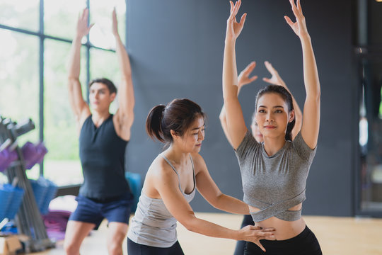 Group of young sporty ethnics people practicing yoga class in gym. Asian woman Trainer help and coaching girl student to correct pose in fitness club