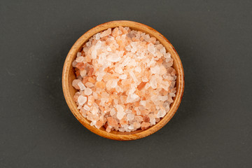 A small wooden bowl filled with pink crystal salt from pakistan on a black background, close up, top view
