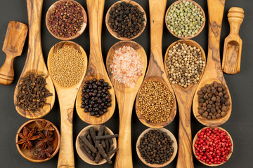 Spice and Food - Background made of many various spices and pepper varieties in small wooden bowls and cooking spoons made of olive wood on a black background