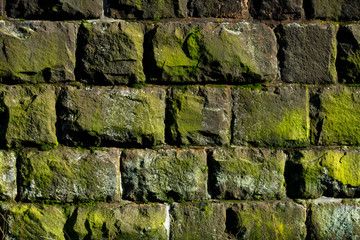 Naklejka premium Mauer Bruchstein alt Moos Algen Pflanzen grün Sonnenlicht Schatten Struktur Hintergrund Vintage Gebäude Sockel Fundament Handwerk