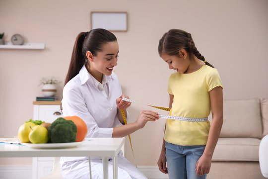 Professional nutritionist measuring waist of little girl in office