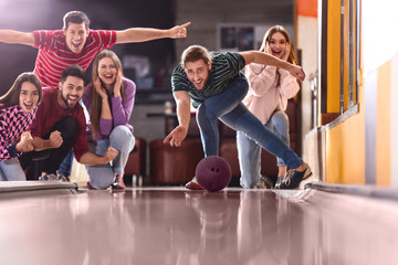 Young man throwing ball and spending time with friends in bowling club