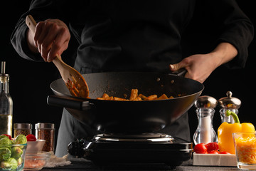 Cooking, the chef cooks pasta with sauce and vegetables in a pan, or wok, against a background of...
