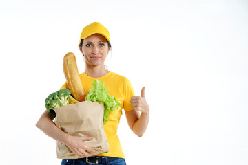 Delivery woman in yellow holding grocery bag and giving thumbs up, on white background