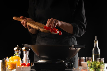 Chef fries Italian pasta with vegetables and meat in a pan, adds cherry tomatoes, freezing in...