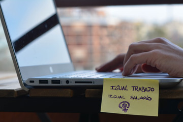 Detail of the hands of a woman working with her laptop and the motto in Spanish "equal job equal salary". Concept: feminism, equality