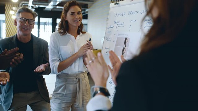 Businesspeople applauding their smiling female colleague after presentation at workplace. Business professionals giving applause at a meeting to colleague in front of whiteboard.