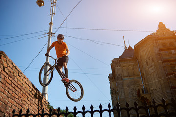 Horizontal snapshot of a freestyle biker jumping from a brick wall making extreme stunt under blue...