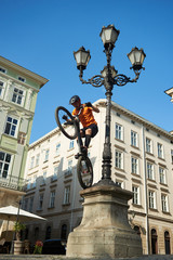 Fototapeta na wymiar Young man is performing extremal trick with his bmx bike, keeping balance on back wheel on a pillar of ancient street lighting, low angle snapshot