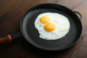 two fried eggs in the pan on wooden background