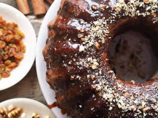 Holiday homemade cakes. Round chocolate muffin, large muffin or chocolate icing cake on a wooden ancient background with nuts, raisins, and cinnamon. Place for text.