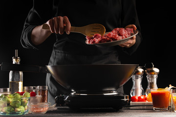 Cooking dishes by the chef, frying fresh pork meat in a pan. Freezing in motion, against the background of vegetables. Gastronomy and cooking. Cooking food