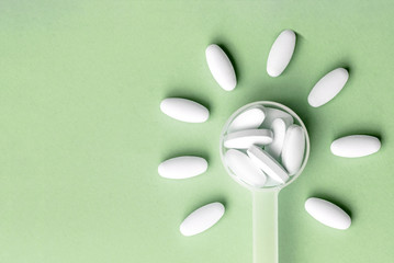 White pills in dosage spoon for drugs in the shape of a flower on a green background, close-up