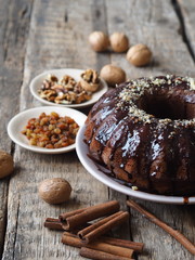 Festive homemade cakes. Round chocolate muffin, large muffin or chocolate icing cake on a wooden ancient background with nuts, raisins, and cinnamon. Place for text.