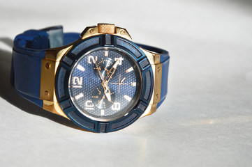 Stylish blue wrist watch on a white background. Round dial in blue and gold colors.