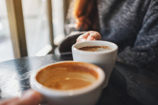 Closeup image of a woman and a man clinking coffee mugs in cafe