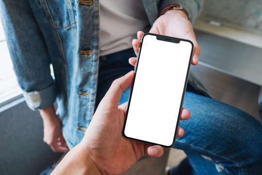 Mockup image of a woman holding and showing white mobile phone with blank black desktop screen to someone
