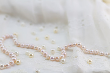 Pearl necklace on lace dress background - selective focus on pink and champagne pearls