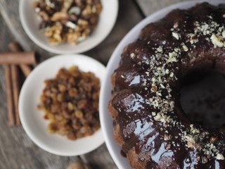 Holiday homemade cakes. Round chocolate muffin, large muffin or chocolate icing cake on a wooden ancient background with nuts, raisins, and cinnamon. Place for text.