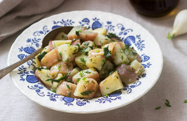 Traditional cold potato salad with onions and herbs on a linen tablecloth background. Rustic style.