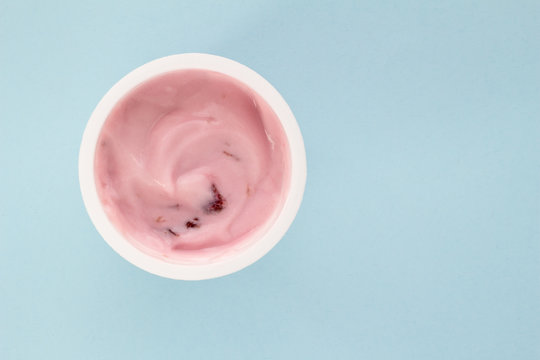 Yogurt in plastic cup close up - top view photo of strawberry yoghurt on pale blue background