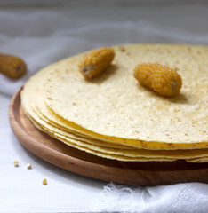 A stack of round corn tortillas on a wooden board and corncobs.