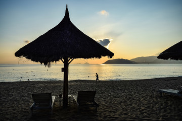 Silhouette of a man on the beach at sunrise and a straw umbrella on vacation