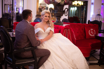Young bride and groom in a cafe. Husband and wife hold each other's hands. Loving couple in a restaurant. Pretty bride and stylish groom. Wedding day. Marriage.