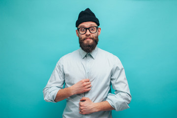Handsome hipster guy with beard smiling happily, dressed casually with black beanie on head isolated over a blue studio background. The concept of people, crazy emotions.