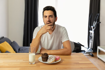 Fototapeta na wymiar Young handsome guy sits at a table and eats donuts.