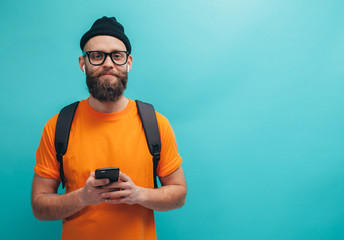 Handsome hipster guy with beard wearing orange t-shirt , types text message on smartphone, isolated...