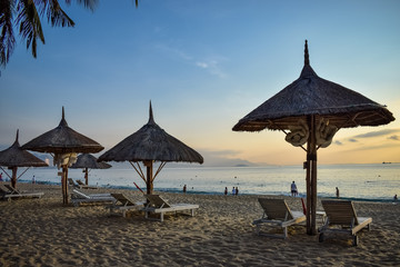 Straw umbrellas on a sandy beach at dawn and wooden deck chairs by the sea