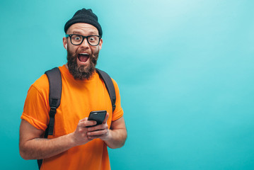 Handsome hipster guy with beard wearing orange t-shirt , types text message on smartphone, isolated...