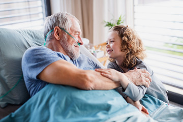 Small girl visiting ill grandfather in hospital room.