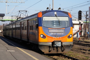 Fototapeta premium The orange and blue electric train at the railway station. Track, poles and supports for current-carrying lines.