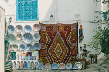 Traditional hand-made Tunisian carpets and painted plates for sale on a street in the blue town of Sidi Bou Said, Tunisia