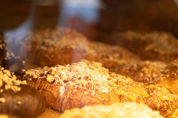 French croissants with streusel in bakery window shop covered with glass. Culinary background for wallpaper or postcard. Horizontal. Close up.