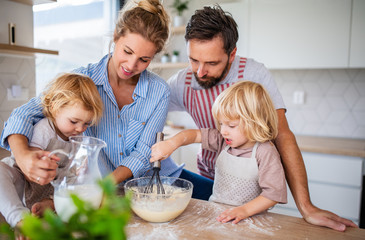 Young family with two small children indoors in kitchen, cooking.